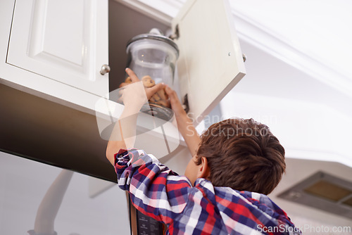 Image of Kitchen, cupboard and cookie jar with boy child reaching for treats for hunger in home from below. Biscuits, food or snack in glass with young kid in apartment, stealing baked goods to eat from back