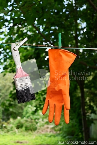 Image of a paint brush and a rubber orange glove hang on a clothesline 