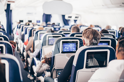 Image of Interior of airplane with passengers on seats and stewardess in uniform walking the aisle, serving people. Commercial economy flight service concept.
