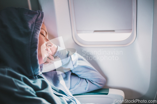 Image of Tired blonde casual caucasian woman wearing sporty hoodie napping on seat while traveling by airplane. Commercial transportation by planes. Authentic image of real people.