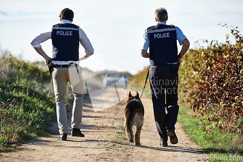 Image of Policeman, dog and walk in field for crime scene or robbery with car for search, safety and law enforcement. Detective, investigation and uniform in outdoor working at countryside with gravel road