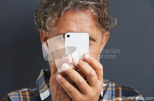 Image of Mature, man and capture a photo with phone in studio and learning about photography on dark background. Smartphone, recording or filming a video for post online to social media for memory of picture