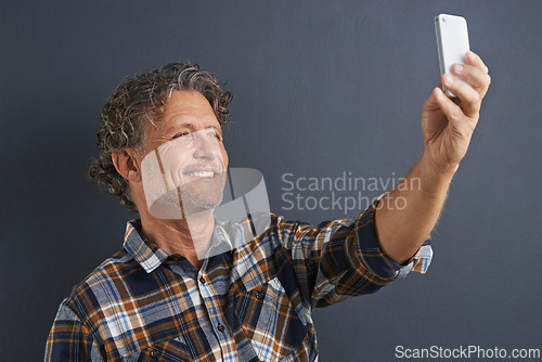 Image of Mature, man and happy selfie in studio and learning about photography on dark background. Filming, video or click record for profile picture and post online to social media with website or blog