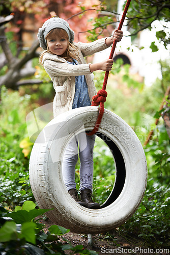 Image of Portrait, young girl and swing in garden, nature and entertainment in playground. Child, freedom and tyre for childhood development in forest, woods or park on weekend or holiday in autumn season