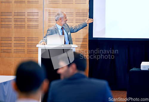 Image of Senior, businessman and leader with presentation on projector for meeting, seminar or conference at office. Man spokesperson, CEO or speaker talking on podium to group, corporate audience or workshop