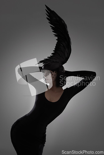 Image of Bird, fashion and art style woman in a studio with head piece, feather hat and abstract with unique creativity. Crow, silhouette and shadow with fantasy and with goth clothes and grey background