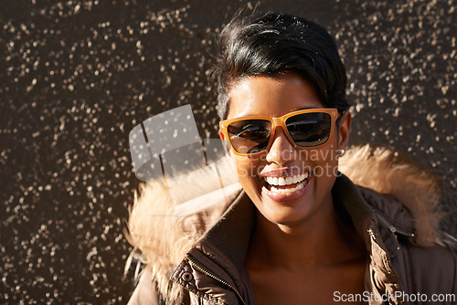 Image of Woman, sunglasses and smile with portrait, sunshine and accessorise for trendy fashion. Model, laugh and jacket with style, happiness and urban outdoor background with grey wall and cool sunrise