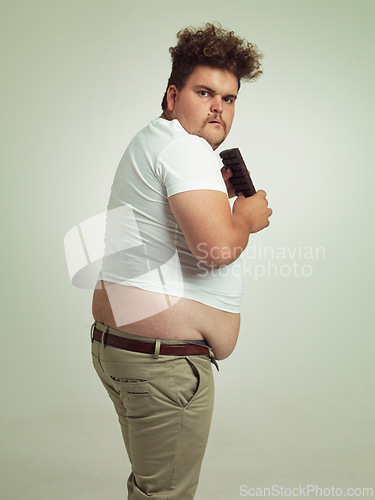 Image of Chocolate, portrait and plus size man with junk food, dessert and candy in a studio. Funny, sweet and unhealthy snack for eating with greed gesture and hungry male person with green background