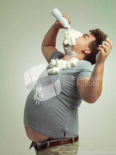 Image of Plus size, eating and man with cream in studio for unhealthy, sugar and sweet snack or dessert. Messy, greedy and hungry plus size male person enjoying whipped dairy product by gray background.