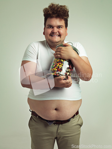 Image of Candy, crazy and portrait of plus size man in studio for luxury snacks, sweets and dessert in container. Comic, funny facial expression and isolated person with glass for unhealthy diet on background