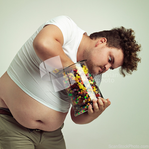 Image of Candy, jar and man in on studio background crazy for luxury snack, sweets or dessert in container. Comic, facial expression and isolated and plus size person with glass for unhealthy diet and sugar