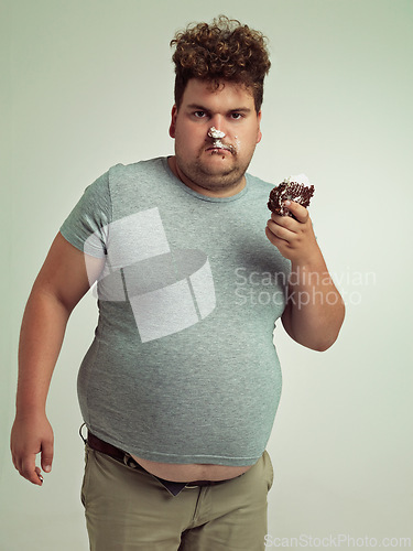 Image of Chocolate cake, portrait and plus size man with grumpy, dessert and candy in a studio. Silly, sweet and unhealthy snack for eating with junk food and hungry person with green background with joke