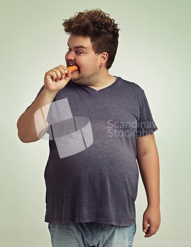 Image of Plus size, diet and man eating carrot for nutrition, health benefit and wellness in studio by white background. Weight loss, vegetable and hungry male person for detox, wellbeing and vegan food