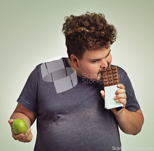 Image of Man, apple and chocolate in studio with choice of junk food, sweet or diet for wellness. Plus size, male person eating and decision, fruit or candy for nutrition, lose weight and healthy lifestyle