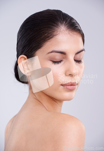 Image of Calm woman, face and skincare with cosmetics or facial treatment on a gray studio background. Young female person, brunette or model with smile in satisfaction for beauty, makeup or spa cosmetology