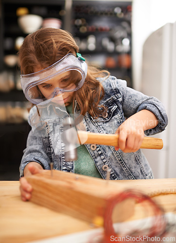 Image of Chilld, construction and hammer a nail in workshop, play and game in kitchen of home. Female person, girl and safety glasses or tool for wood project or hobby, carpentry and remodeling or manufacture