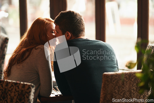 Image of Couple, happiness and kiss on date at restaurant for bonding, romance or healthy relationship with rear view. Man, woman and affection at coffee shop with smile, trust or love on anniversary vacation