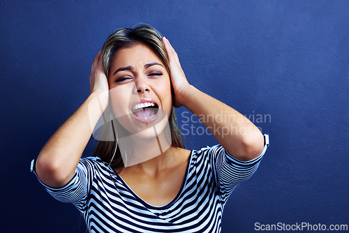 Image of Woman, noise and cover ears in studio with stress, mental health and shouting with anxiety by blue background. Girl, person and model with tinnitus, frustrated and stop sound with hands on head