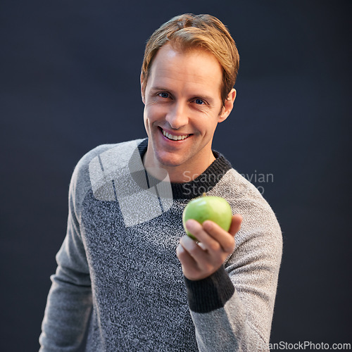 Image of Man, apple and smile in studio portrait with choice for detox, diet or health by dark background. Person, model and happy with green fruit with pride for decision, vegan nutrition and organic snack