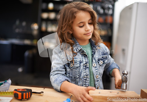 Image of Girl, carpentry and hammer a nail in workshop, play and game in kitchen of home. Female person, child and equipment or tool for wood project or hobby, construction and remodeling or manufacture