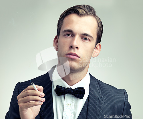 Image of Portrait, suit or young gentleman smoking a cigarette in studio, confidence or vintage fashion by white background. Face, serious and man in retro clothes or tuxedo, bow tie and class at formal event