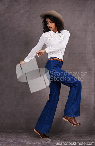 Image of Woman, fashion and western clothes in studio, wild west and country style on Indian model. Jumping, confident strong female person with trendy hat accessory, culture and isolated on backdrop