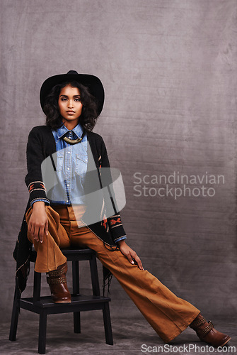 Image of Portrait, cowgirl or woman in studio, wild west culture and cool fashion in clothing on grey background. Young female person, western lady and stylish model with pride, boho style and chair stool