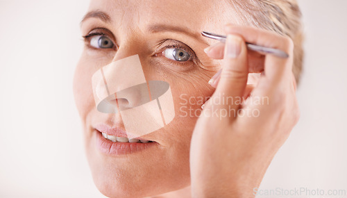 Image of Beauty, tweezers and portrait of a mature woman on white background for facial grooming or hair removal. Spa, salon and face of female model in studio plucking or tweezing eyebrows for skincare glow