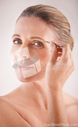 Image of Eyebrows, tweezers and portrait of a mature model on white background for facial grooming or hair removal. Beauty, salon and face of female person isolated in studio plucking or tweezing for skincare