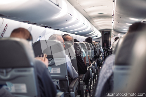 Image of Interior of airplane with passengers on seats and stewardess in uniform walking the aisle, serving people. Commercial economy flight service concept.