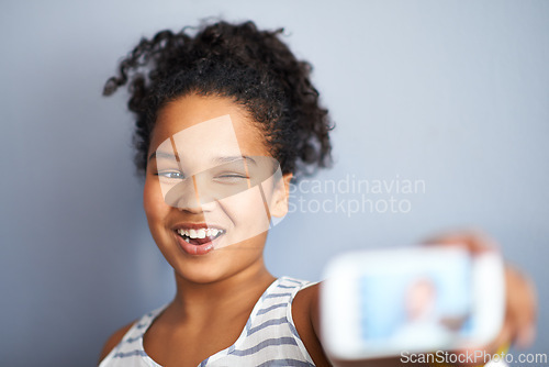 Image of Young girl, selfie and wink in studio for happiness, closeup and vibrant teen by grey background. Child, smile and excited teenager with profile picture, technology and update on social media