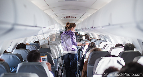 Image of Interior of airplane with passengers on seats and female traveler walking the aisle. Commercial economy flight service concept.