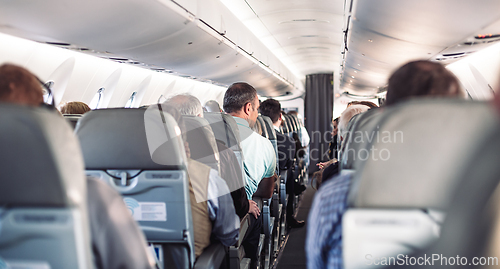 Image of Interior of airplane with passengers on seats and stewardess in uniform walking the aisle, serving people. Commercial economy flight service concept.