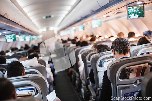 Image of Interior of airplane with passengers on seats and stewardess in uniform walking the aisle, serving people. Commercial economy flight service concept.