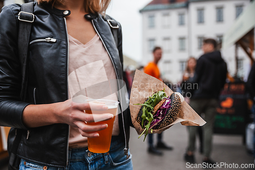 Image of Close up of woman hands holding delicious organic salmon vegetarian burger and homebrewed IPA beer on open air beer an burger urban street food festival in Ljubljana, Slovenia.