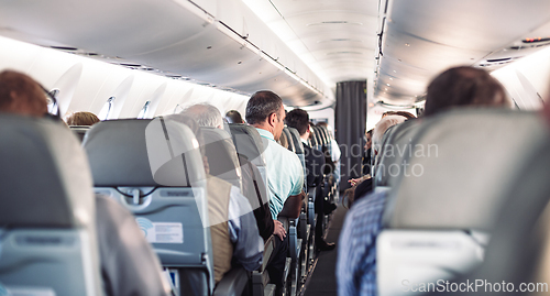 Image of Interior of airplane with passengers on seats and stewardess in uniform walking the aisle, serving people. Commercial economy flight service concept.