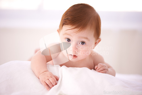 Image of Portrait, care and curious baby on bed, tummy time for child development and play in nursery comfort. Girl, infant or newborn wellness in family home for childcare, crawl or kid learning for growth