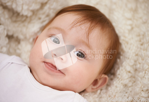 Image of Happy, cute and face of baby on blanket playing for child development and curious facial expression. Smile, sweet and girl kid, infant or newborn relaxing and laying on bed in nursery room at home.