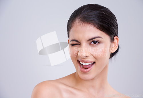Image of Excited woman, portrait and wink with skincare in satisfaction for beauty, cosmetics or facial treatment on a gray studio background. Happy female person, brunette or model flirting on mockup space