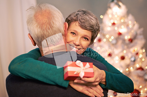 Image of Christmas, portrait and gift with senior couple with love, care and support together in a home on holiday. Tree, retirement and marriage with a smile and hug in a house with celebration and present