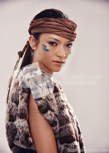 Image of Portrait, girl and Native American culture in studio with warrior makeup, confidence and tribe style. Indigenous fashion, face paint and serious woman in First Nations clothes on white background