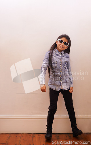 Image of Girl, child and fashion or sunglasses for style and looking cool on a wall background at home. Happy portrait of a kid or child with trendy clothes, casual and accessory or shades for fun indoors