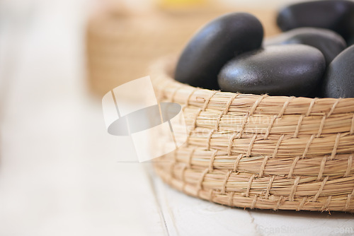 Image of Stone, massage and closeup on basket in spa for luxury service in hospitality at hotel on holiday or vacation. Rocks, container and object for wellness treatment on table or detail of pebble