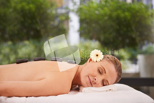 Image of Woman, hands and hot stone massage at spa with eyes closed, flower for natural treatment and wellness with zen. Calm, peace and luxury with warm rocks for detox, self care and holistic healing