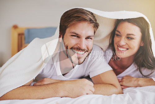 Image of Smile, love and couple with blanket for relaxing, bonding and resting on bed together at home. Happy, romantic and young man and woman laying with duvet in bedroom at hotel, house or apartment.