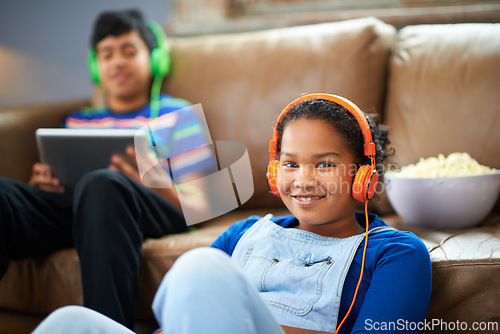 Image of Tablet, children and portrait of girl with headphones in streaming, music or audio book with her brother at home. Kids, family and siblings in living room with digital, app or radio, relax or bonding