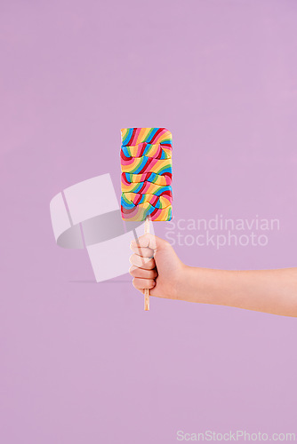 Image of Hand, lollipop and candy in studio for dessert sweets on purple background for carnival snack, hungry or mockup space. Fingers, stick and treats for party food or sugar eating, birthday or unhealthy