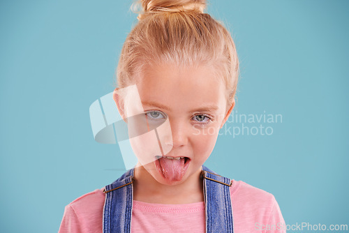 Image of Kid, portrait and tongue out in studio for silly, goofy and playful facial expression with blue background. Child, crazy and funny face of young girl for comic gesture, humor and joking for comedy