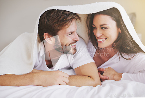 Image of Happy, love and couple in conversation with blanket for relaxing, bonding and resting on bed together. Happy, romantic and young man and woman laying with duvet in bedroom at hotel, home or apartment