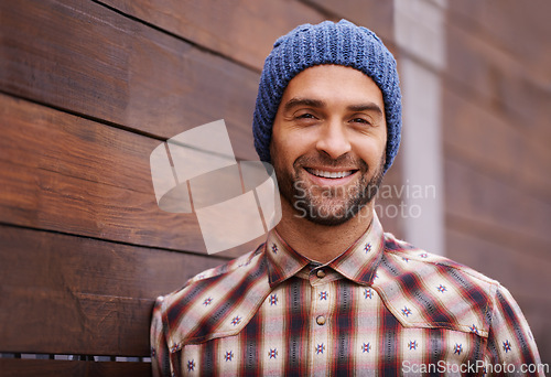 Image of Portrait, smile and man on wood wall background outdoor in casual clothes, outfit or apparel. Face, happy and stylish person in beanie, shirt and trendy fashion for profile picture with hat in Spain